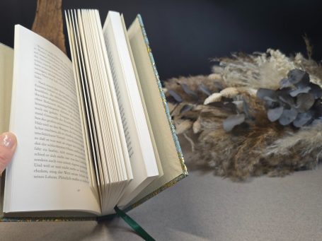 Das Parfum - Patrick Süskind Ein aufgeschlagenes Buch mit einem Blumenarrangement daneben.