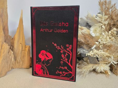 Das Buch "Die Geisha" von Arthur Golden mit rotem Umschlag und dekorativen Elementen.