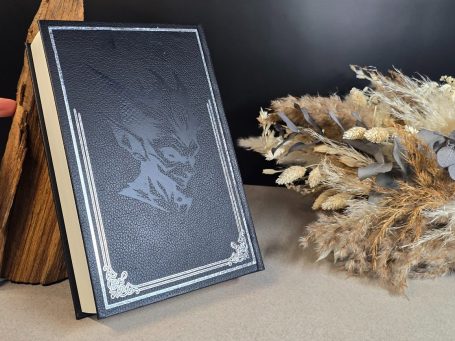 The Witcher - Kurzgeschichten - Andrzej Sapkowski&nbsp; Schwarzes Buch mit dekorativem Einband neben trockenen Blumen und Holzstück.