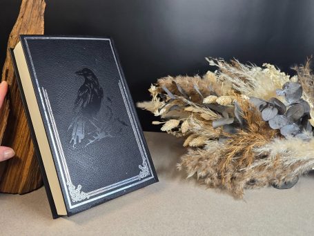 The Witcher - Kurzgeschichten - Andrzej Sapkowski&nbsp; Schwarzes Buch mit Rabenmotiv neben einem Arrangement aus Trockenblumen.