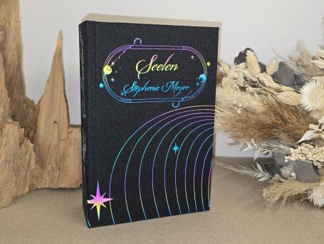 Seelen - Stephenie Meyer Schwarzes Buch mit bunten Sternen und geschwungenen Linien, daneben dekorative Pflanzen.