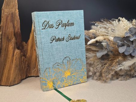 Das Parfum - Patrick Süskind
Ein blaues Buch mit goldenen Blumenmotiven und dem Titel „Das Parfum"