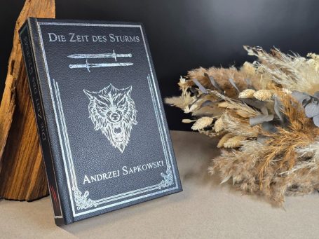 The Witcher - Kurzgeschichten - Andrzej Sapkowski&nbsp; Ein Buch mit einem Wolf-Emblem auf dem Cover, daneben Trockenblumenarrangement.