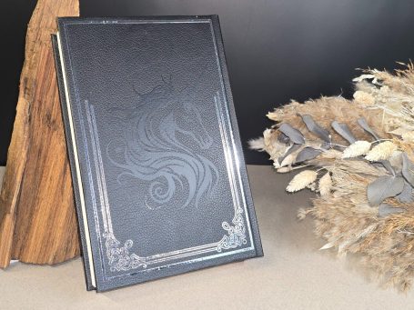 The Witcher - Pentalogie - Andrezj Sapkowski Schwarzes Buch mit verziertem Rand und floralem Hintergrund.