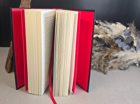 The Witcher - Pentalogie - Andrezj Sapkowski Ein geöffnetes Buch mit weißen Seiten und rotem Lesezeichen auf einem neutralen Hintergrund.