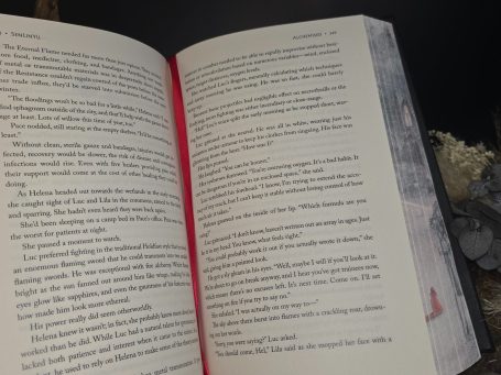 Alchemised - SenLinYu 
Ein geöffnetes Buch mit rotem Schnitt, Text in schwarzer Schrift und Illustrationen.