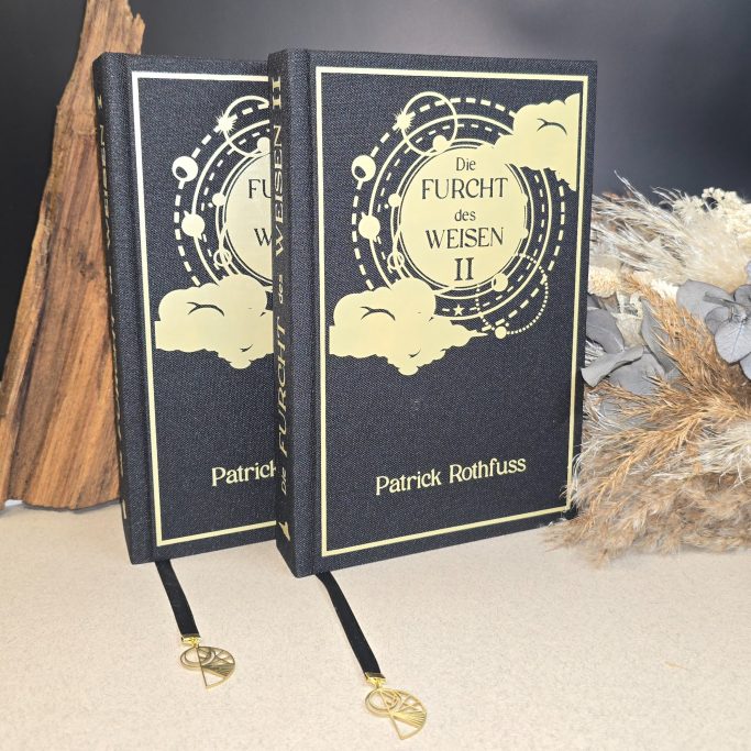 Zwei schwarze Bücher mit goldfarbener Schrift und Verzierungen auf einem Tisch.